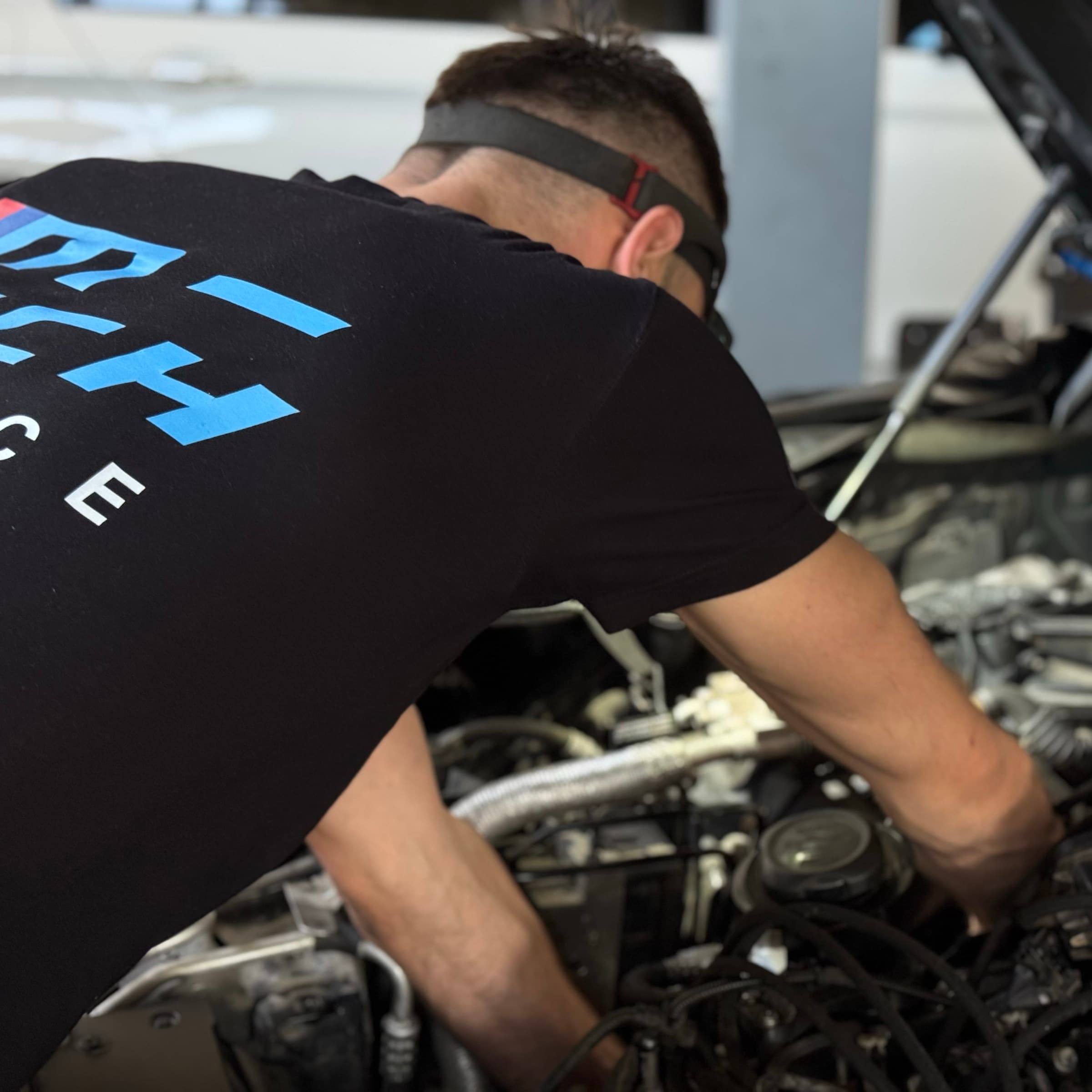 Майстер M-Tech у фірмовій футболці працює під капотом BMW